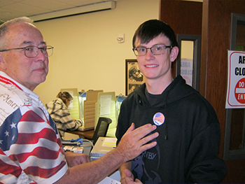 2 people in the photo looking at camera (one younger man with an I voted sticker).