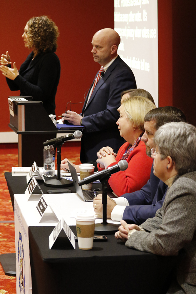 EAC Commissioners Matt Masterson and Christy McCormick, EAC Executive Director Brian Newby and two other speaker form a panel in front of room. A female translator is also present in the photo.