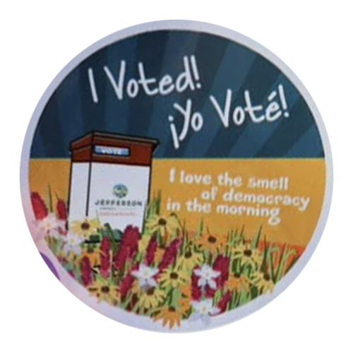 A circular “I Voted! ¡Yo Voté!” design with a ballot drop box labeled for Jefferson County, surrounded by colorful wildflowers and a sunrise over a field, with the phrase “I love the smell of democracy in the morning.”